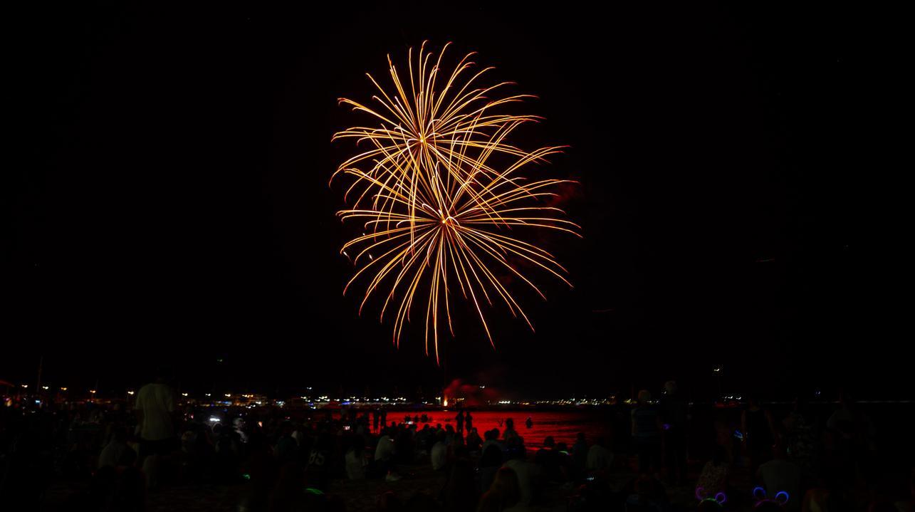 A crowd on Rockingham beach looks up and watches as golden fireworks explode.